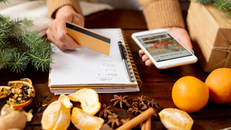 Młoda klientka trzyma kartę kredytową i smartfon nad stołem, zamierzając zamówić prezenty świąteczne dla rodziny