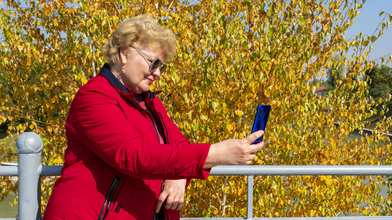 Kaukaski starsza kobieta w czerwonej kurtce za pomocą smartfona w parku