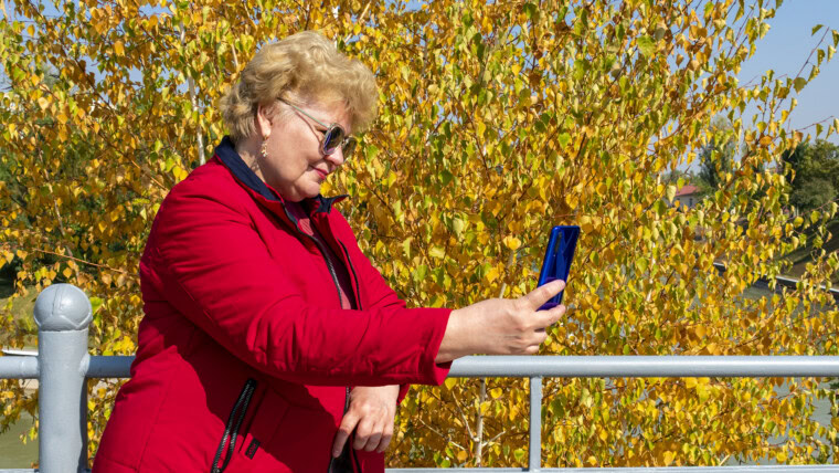Kaukaski starsza kobieta w czerwonej kurtce za pomocą smartfona w parku