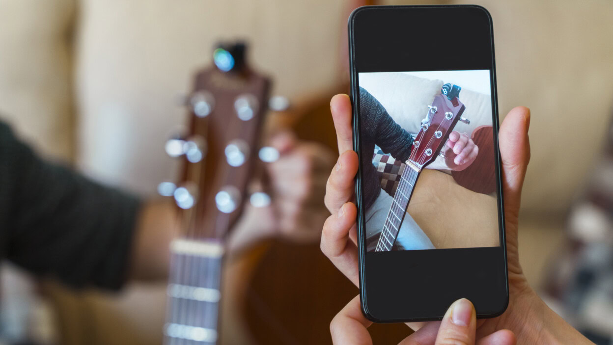 Przycięte ręce kobiety fotografującej mężczyznę trzymającego gitarę