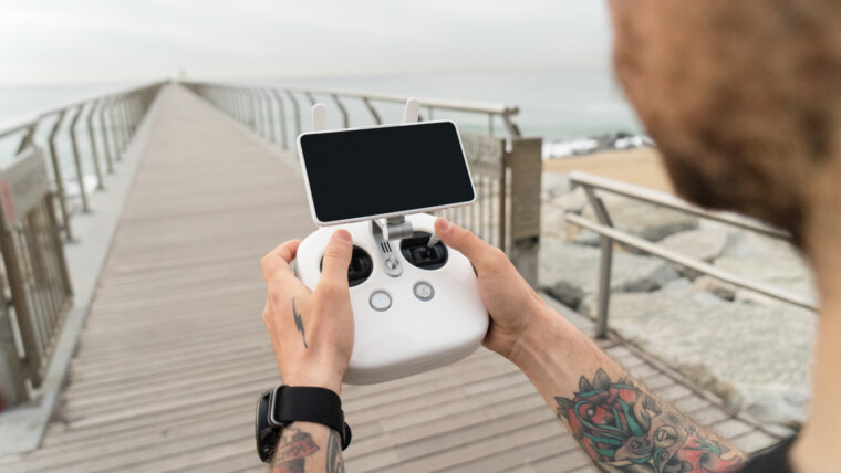 Młody profesjonalny lub amator fotograf lub pilot drona trzyma panel zdalnego sterowania z ekranem i elementami sterującymi gotowymi do lotu dronem w powietrzu, aby zobaczyć ptasi punkt widzenia.