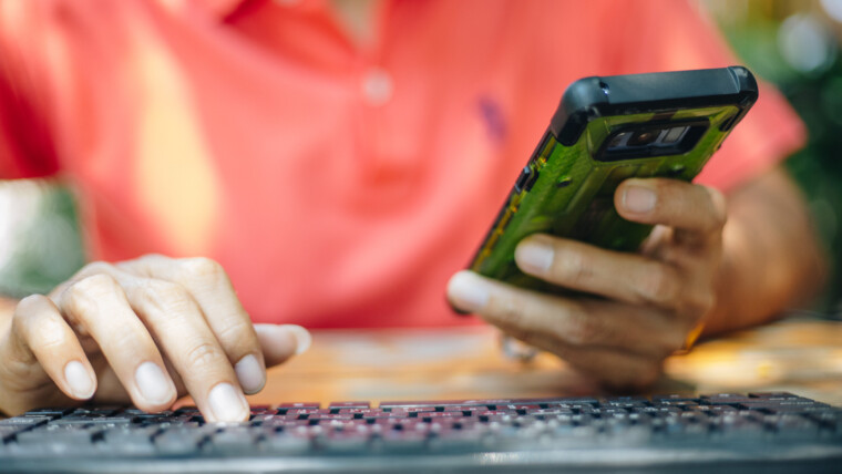 Środkowa sekcja mężczyzny używającego telefonu komórkowego i komputera na stole
