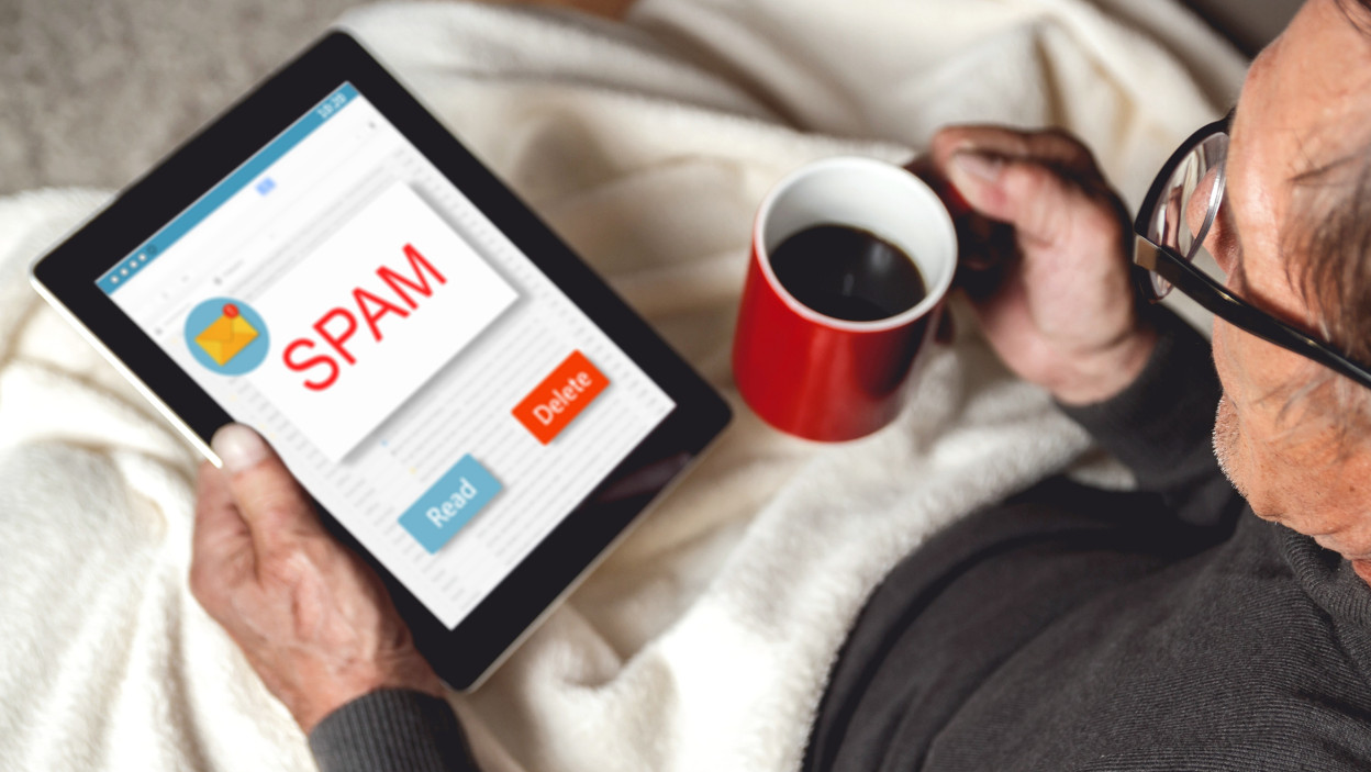 Senior z okularowym siedząc na kanapie z tabletem i czerwoną filiżanką kawy w rękach.