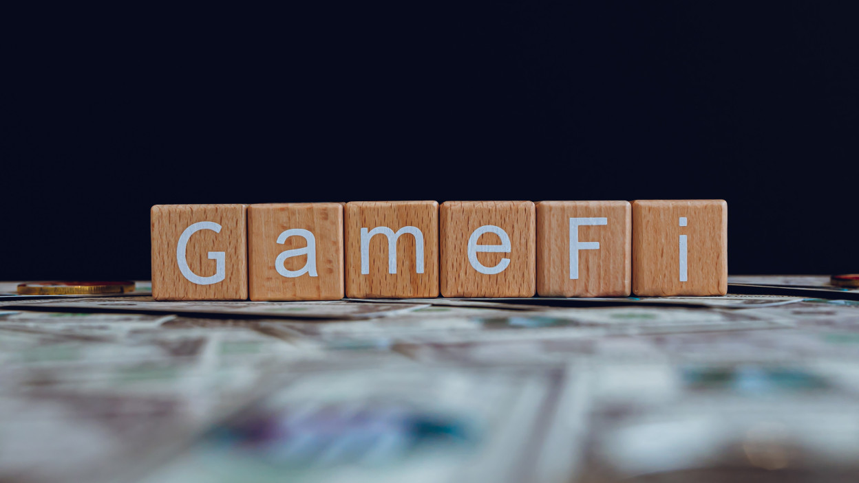 Drewniane klocki z tekstem GameFi na czarnym tle i banknotami kryptograficznymi rozrzuconymi na gro