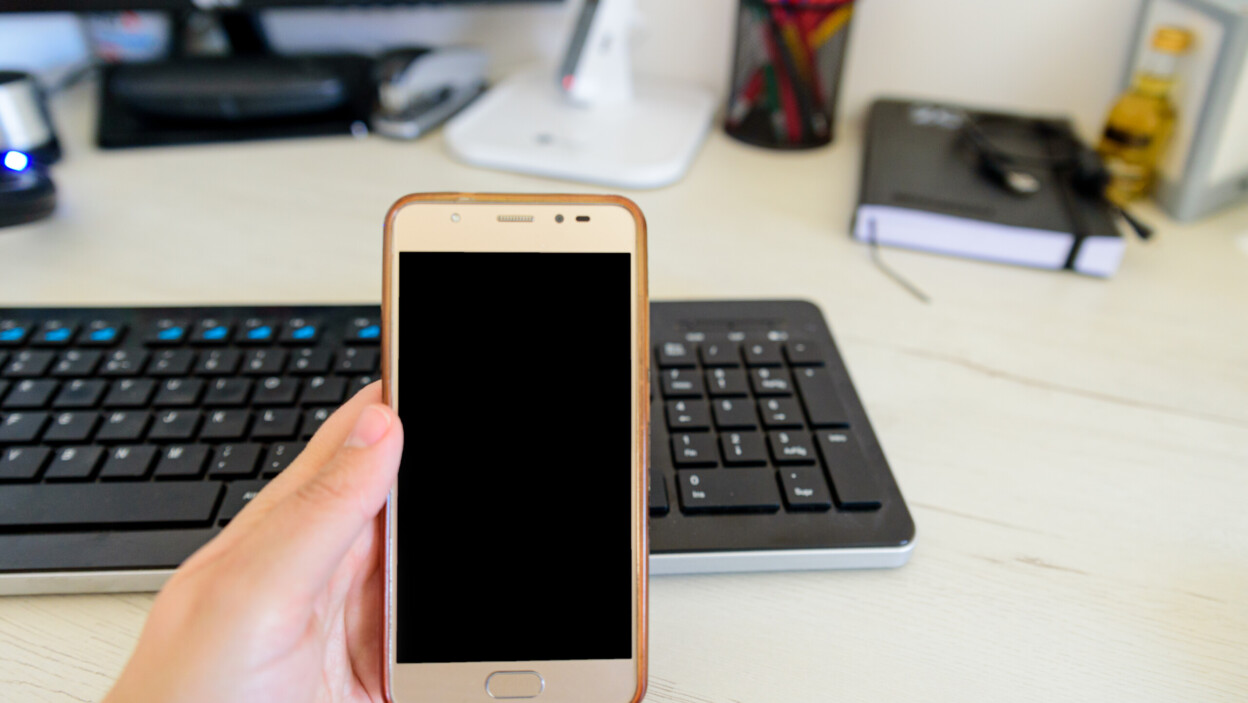 Przycięte ręce osoby używającej telefonu na stole