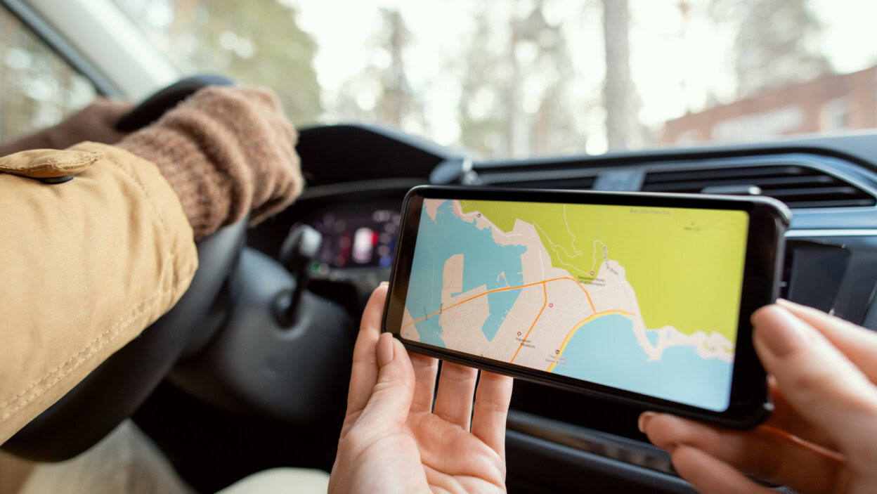 Ręce młodej kobiety siedzącej przez kierowcę i trzymającej smartfona z mapą miejsca, w którym ona i jej mąż podróżują samochodem