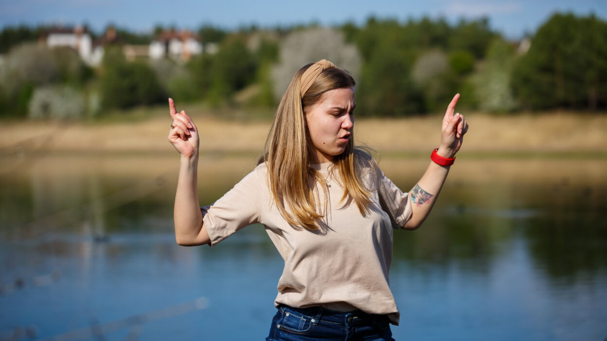 Dziewczyna tańczy w pobliżu jeziora, słoneczna pogoda. Młoda kobieta raduje się życiem, tańczy i śpiewa. Ma dobry nastrój i uśmiech na twarzy.