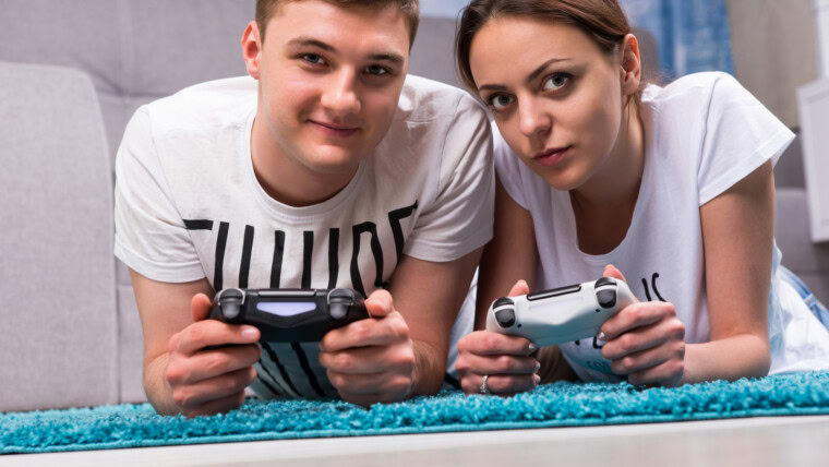 Modna para leżąca na dywanie w salonie, grająca w gry wideo, patrząca w stronę kamery