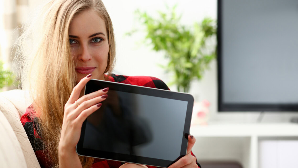 Ładna blond młoda kobieta trzyma laptopa w ramionach siedzi na kanapie