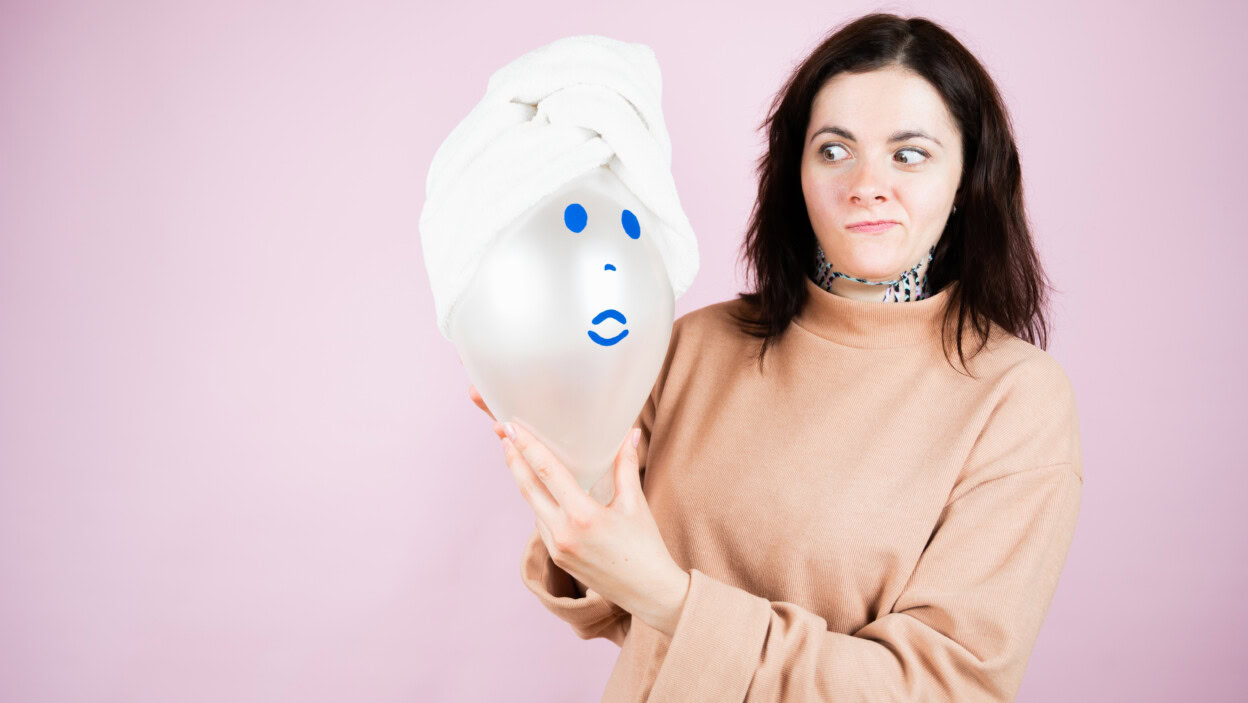 Emocjonalna kobieta trzyma balon z imitacją kobiecej twarzy. Spa, medycyna, opieka zdrowotna, leczenie, koncepcja piękna.