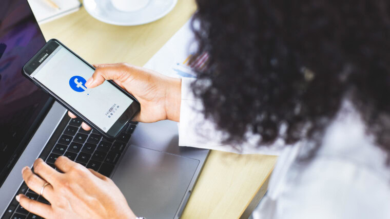 Bangkok/Tajlandia – 06 sierpnia 2021: Przedsiębiorcy siedzący w biurze, pracujący z komputerem, trzymają systemy operacyjne smartfonów z logo Facebooka, najpopularniejszej aplikacji sieci społecznościowej.