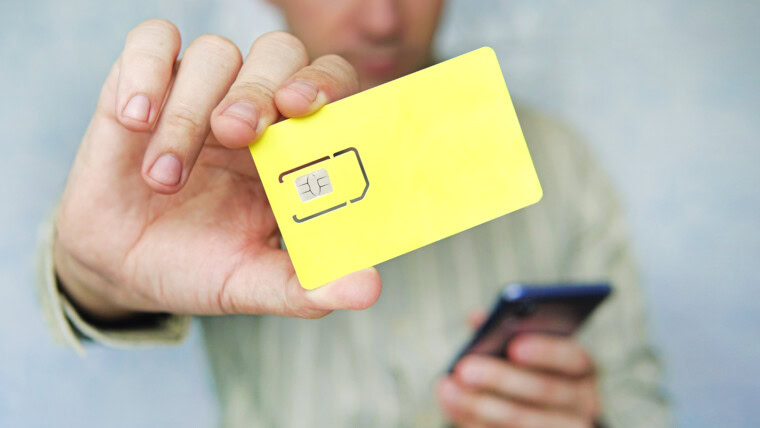 Mężczyzna trzyma w dłoni żółtą kartę SIM i telefon komórkowy. wolne miejsce na projekt i tekst