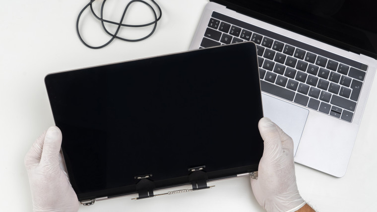 Mężczyzna wymienił zepsuty monitor na laptopie i trzyma go w dłoniach w jasnym białym pokoju
