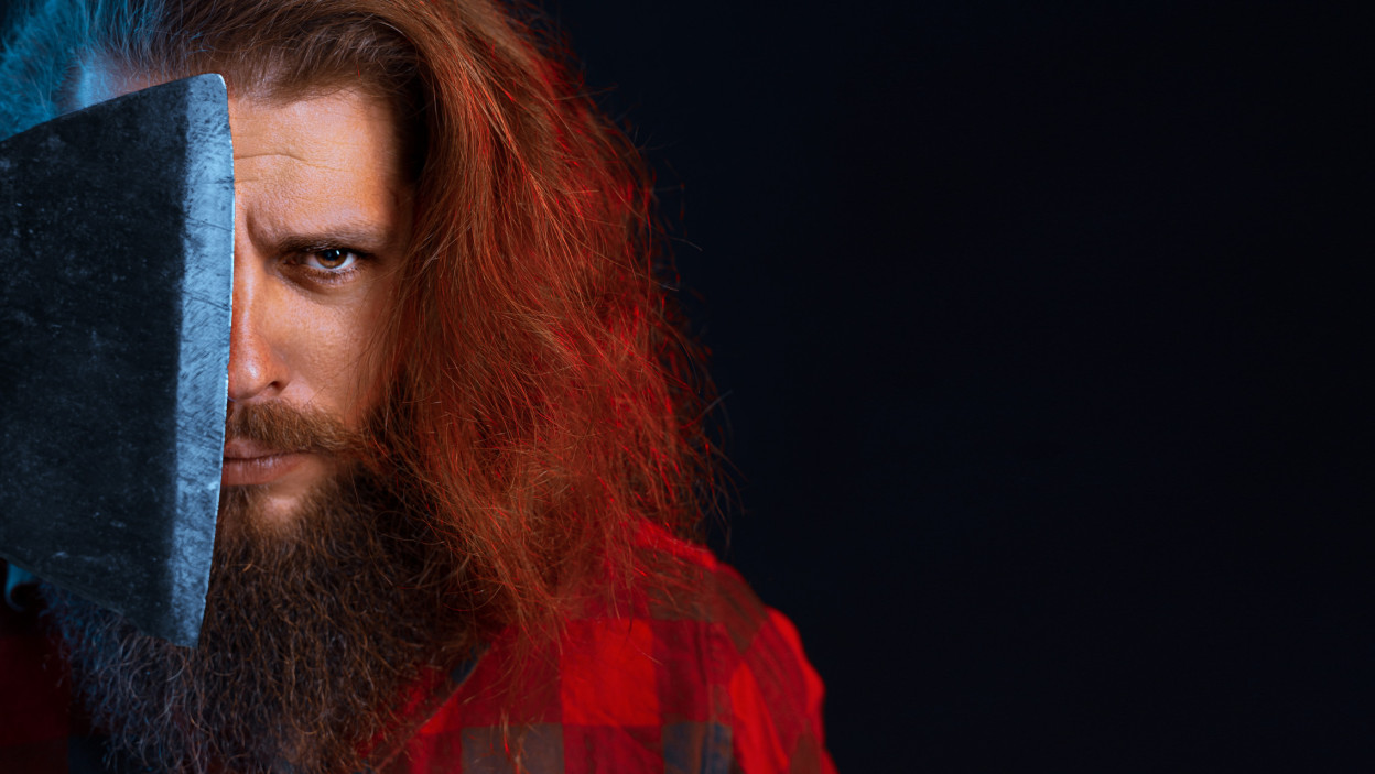 Bliska portret brodatego drwala poważnego mężczyzny w kraciastej koszuli z długimi włosami trzyma starą siekierę