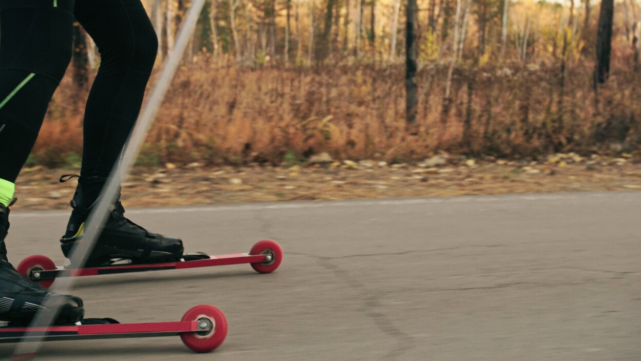 Szkolenie sportowca na wrotkach biathlonowych na nartorolkach z kijkami narciarskimi w hełmie