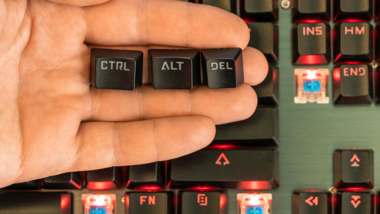 męska ręka trzyma na dłoni trzy klawisze - ctrl alt del nad czarną podświetlaną klawiaturą