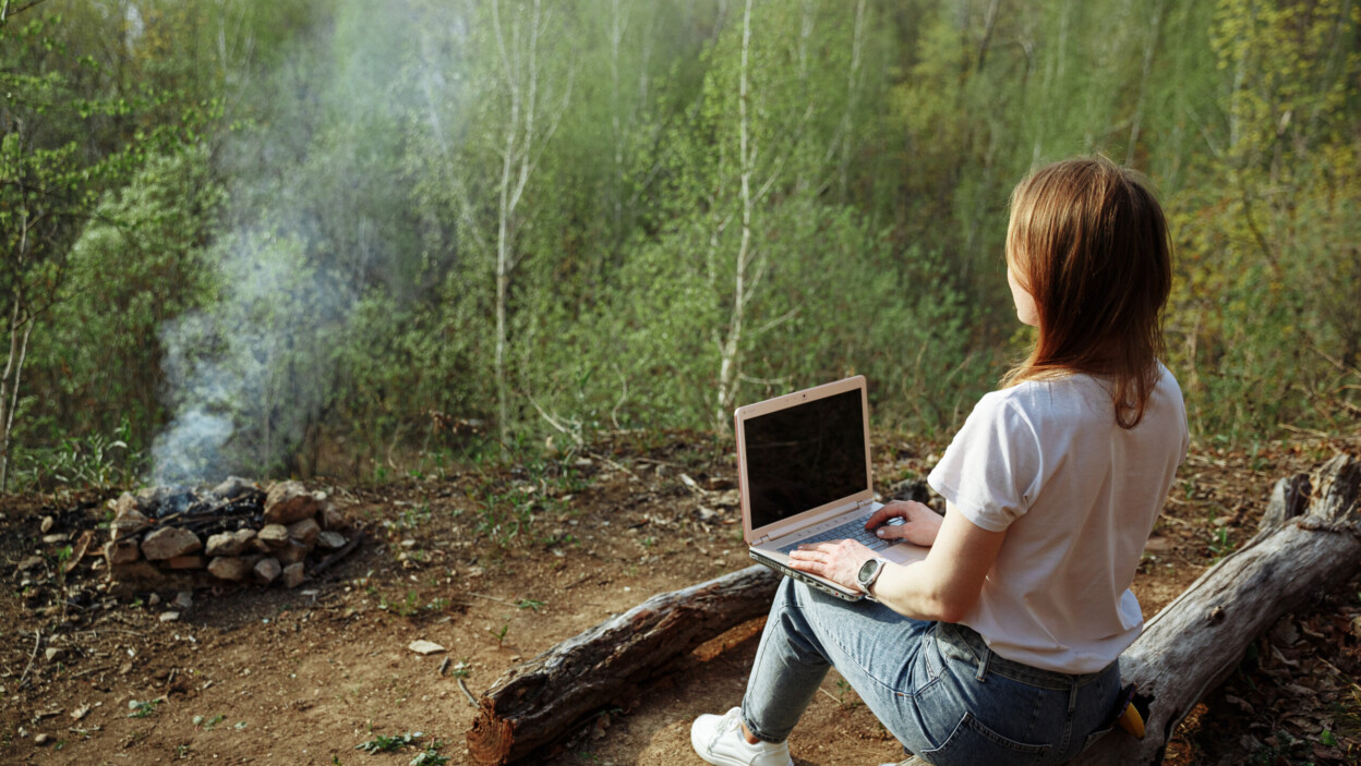 Freelancer siedzi na kłodzie i pracuje na swoim komputerze w lesie przy ognisku Koncepcja pracy zdalnej