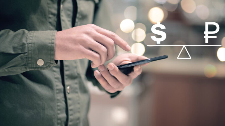 On the scales the ruble and the dollar Man holding a phone in his hand