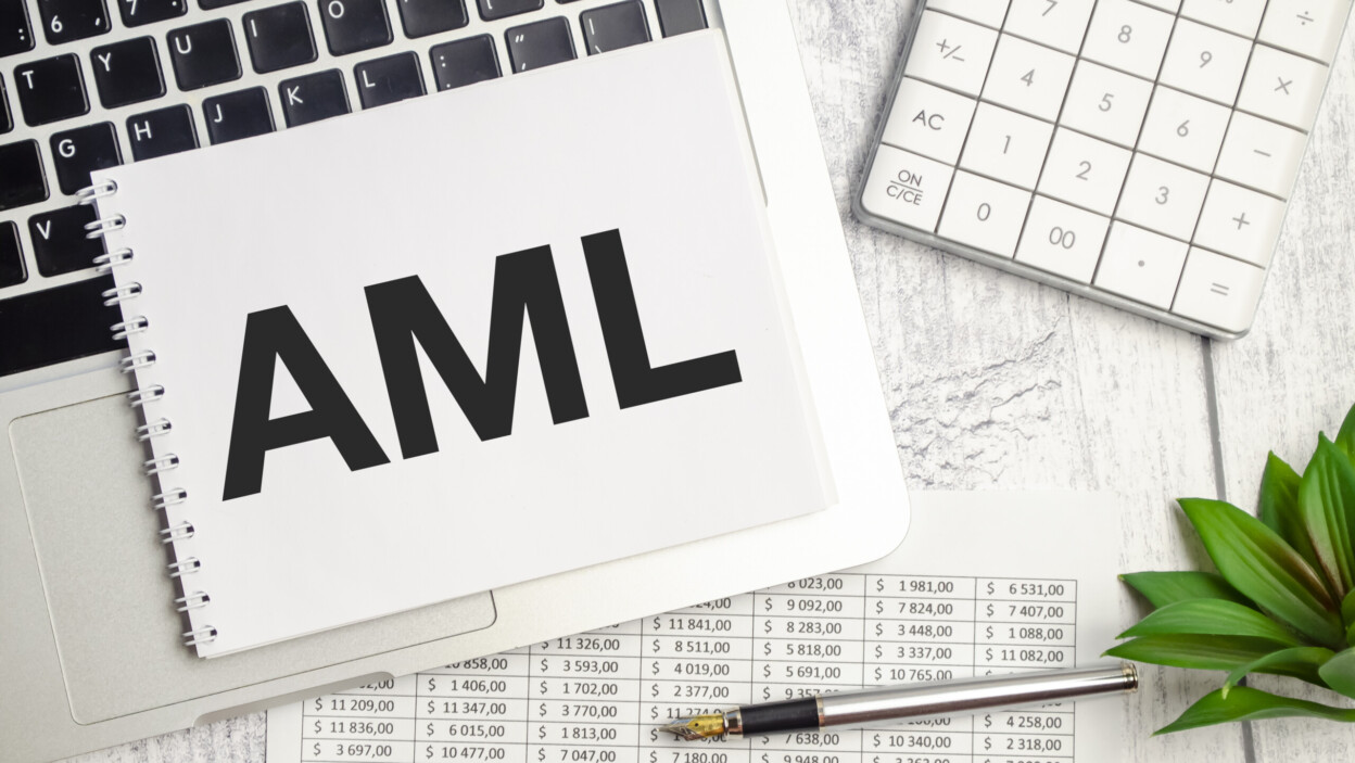 Tekst AML AntiMoney Laundering na notatniku i laptopie na drewnianym tle