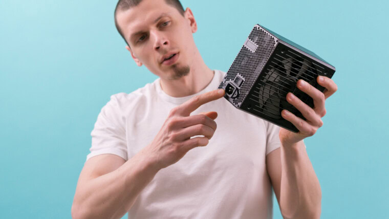 Mężczyzna pokazuje palcem wskazującym złącze zasilacza komputera na niebieskim tle Ręka Elektryczność Elektroniczne elementy zasilania Połączenie Sprzęt Jednostka Elektryczna