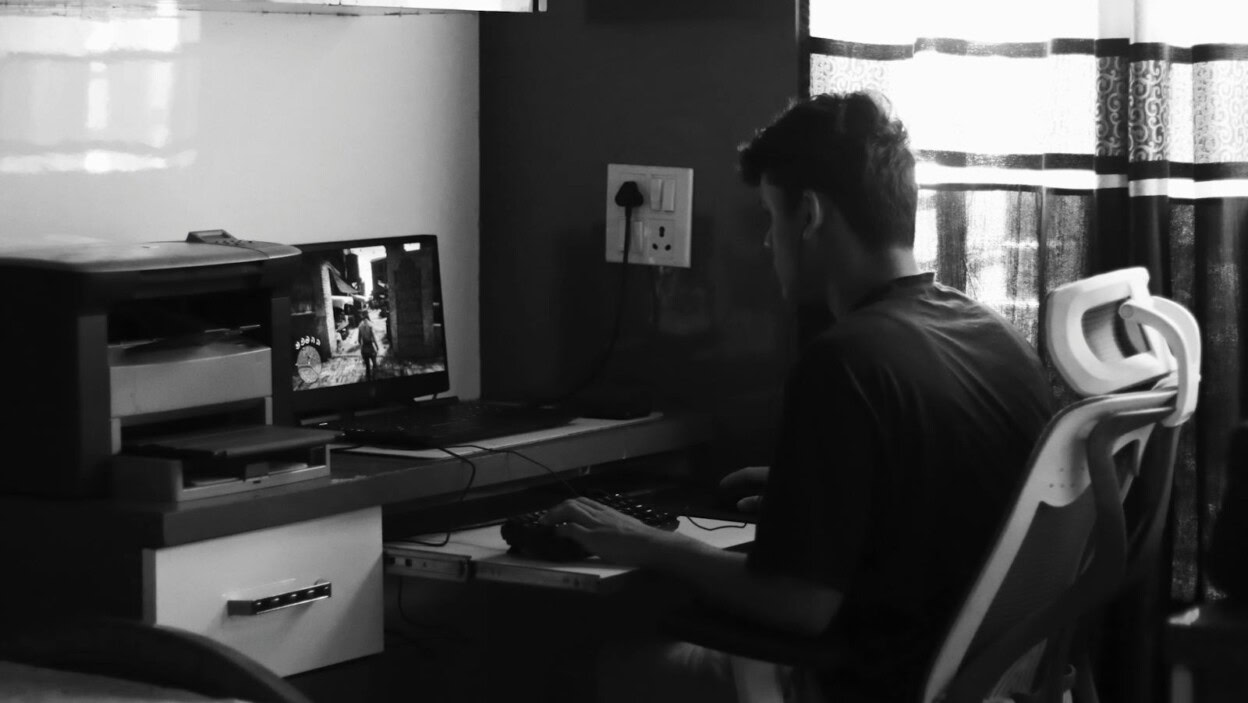 A black and white image of a teenager gaming at a home office desk.