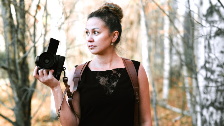 Dziewczyna fotograf w czarnej długiej sukience z rozładunkiem na dwa aparaty z lustrzanką i kamerą filmową