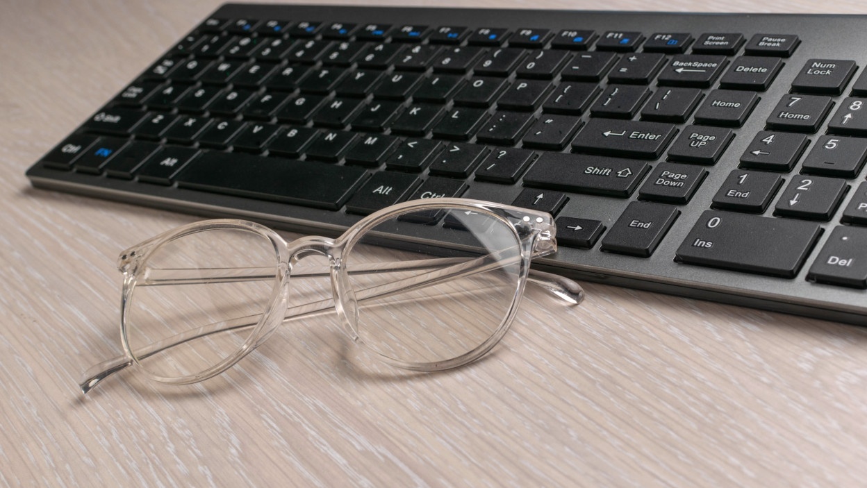Jasne okulary i czarna bezprzewodowa klawiatura na lekkim drewnianym biurku