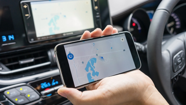 Mężczyzna w samochodzie i gospodarstwa czarny telefon komórkowy z nawigacją gps mapa, stonowanych o zachodzie słońca.