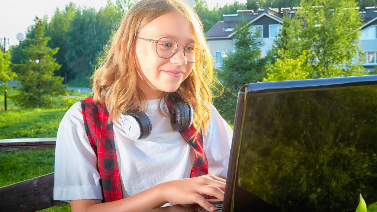 Młoda dziewczyna pisze na laptopie na świeżym powietrzu w słonecznym otoczeniu otoczonej zielenią
