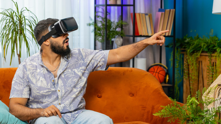Indyjski mężczyzna używający wirtualnej rzeczywistości futurystycznej technologii słuchawki grać w symulację 3D gry wideo w domu