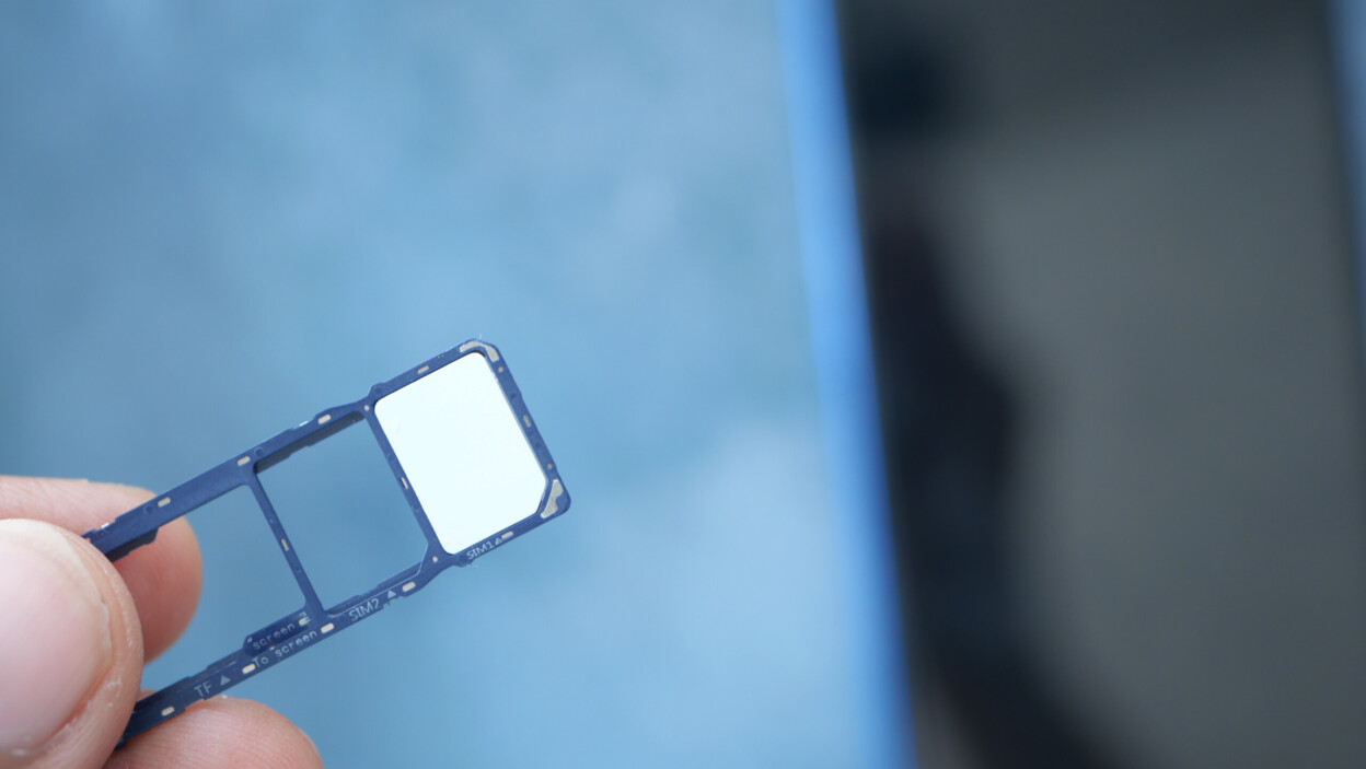 Ręka trzymająca tacę z kartą SIM ze smartfonem w tle