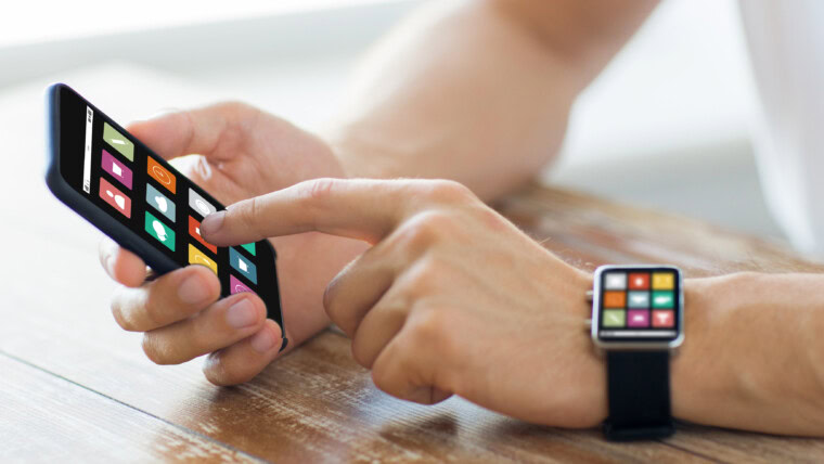 koncepcja biznesu, technologii, multimediów i ludzi - zbliżenie męskich rąk na drewnianym stole, trzymając smartfon i nosząc inteligentny zegarek z ikonami menu na ekranach