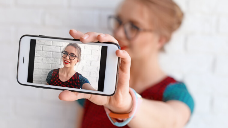 Atrakcyjna młoda kobieta biorąc selfie w pobliżu zbliżenie ściany z cegły