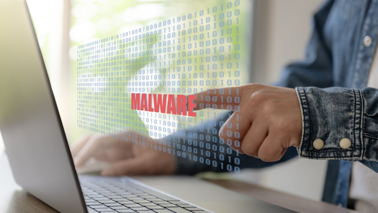 Biznesmen pracuje z laptopem i ręcznie uderza w tekst Malware