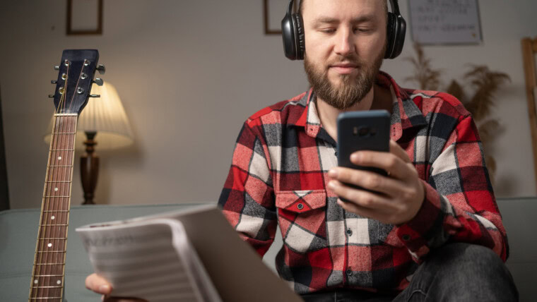 Mężczyzna z gitarą w słuchawkach słuchający lekcji muzyki online Kaukaz mężczyzna młody gitarzysta w domu