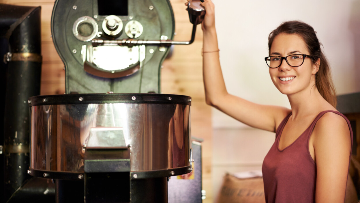 Ekspres do kawy, palarnia i portret baristki w kuchni kawiarni podczas parzenia lub obsługi gości. Sprzęt do serwowania kofeiny i uśmiech kelnerki w restauracji oferującej świeże napoje na sprzedaż.