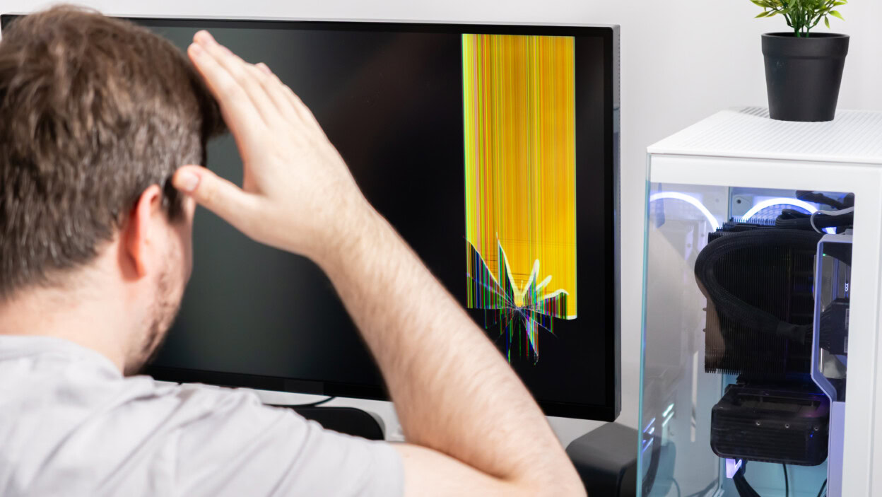 Man reacts with dismay to a broken computer monitor displaying vivid colored lines representing tech failure device damage and user frustration