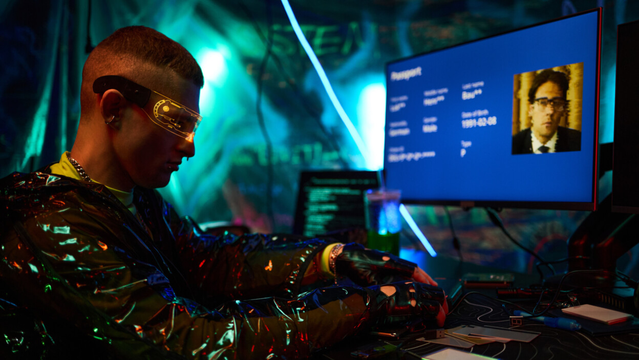 Young caucasian man hacking computer system in dark room with futuristic lighting