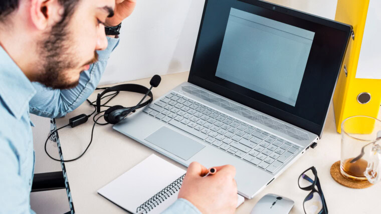 Cz?owiek robienie notatek w notebooku podczas korzystania z laptopa w domu M?oda freelancer pi?mie szczegó?y na ksi??ce