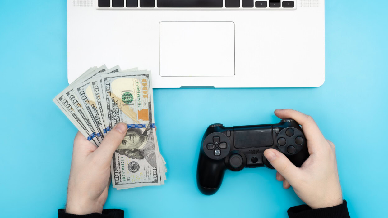 Gamepad i pieniądze w męskich rękach na niebieskim tle widok z góry na koncepcję uzależnienia od gier wideo