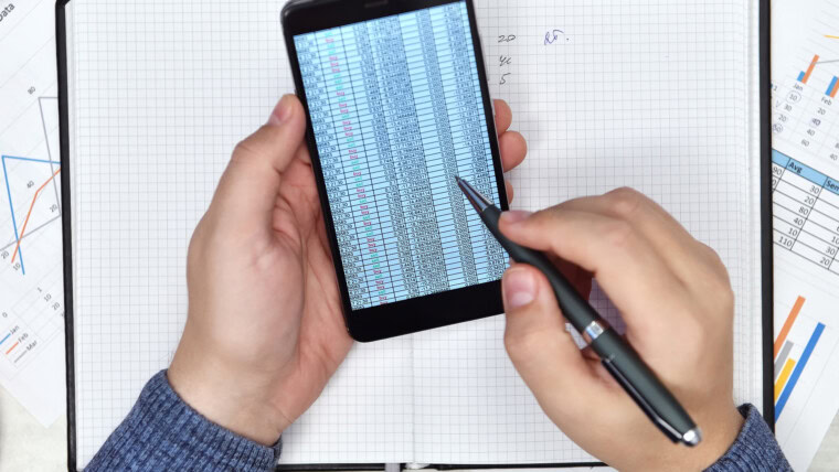 Ręce księgowego za pomocą telefonu komórkowego z raportem finansowym
