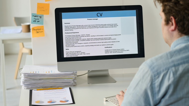 Widok z tyłu młodego biznesmena siedzącego w miejscu pracy i korzystającego z komputera do opublikowania swojego CV w Internecie