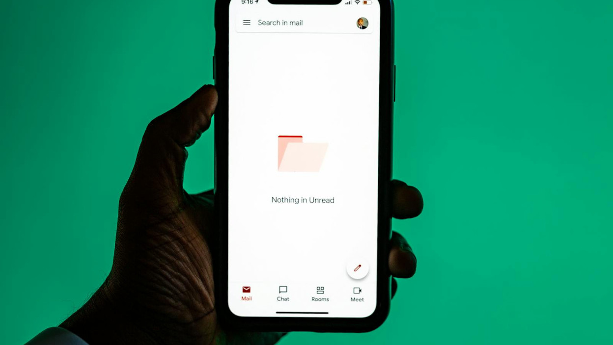 Close-up of a hand holding a smartphone displaying email app against a green background.