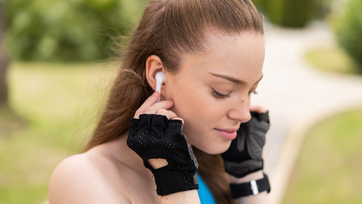 Młoda ładna dziewczyna na zewnątrz, ubrana w odzież sportową i słuchająca muzyki w słuchawkach bezprzewodowych