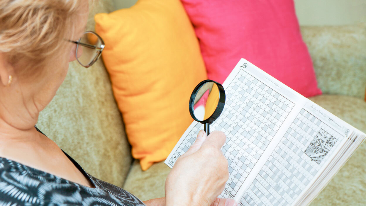 Starsza kobieta rozwiązuje krzyżówki za pomocą szkła powiększającego