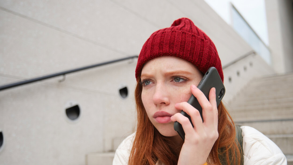 Rudowłosa dziewczyna z zatroskaną twarzą, wyglądającą na zmartwioną, odbierając telefon, słyszy złe wieści