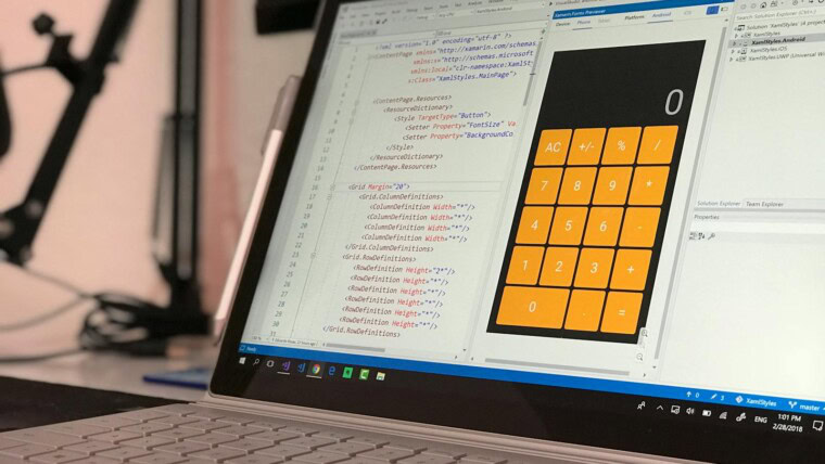 A laptop screen shows a coding application with a calculator design in a tech office setting.