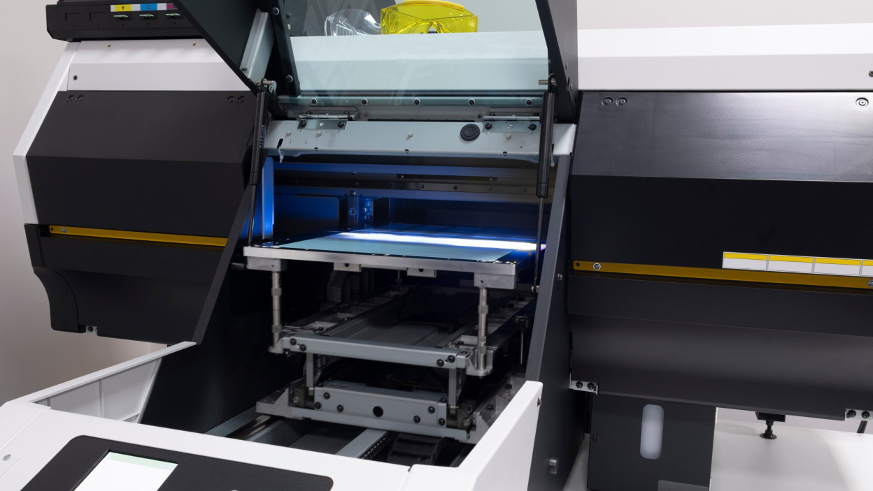 Duża drukarka UV nakłada warstwy farby na arkusz papieru i utwardza je za pomocą ultrafioletu w drukarni.