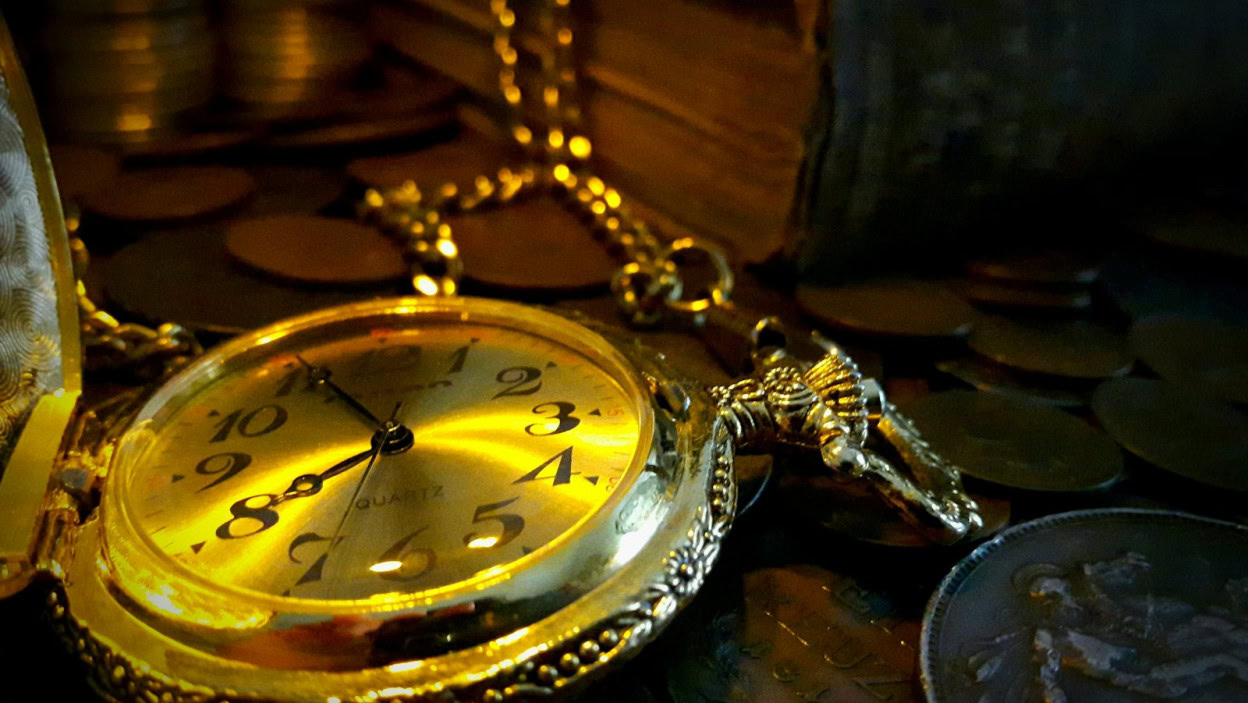 Antique pocket watch surrounded by coins and books