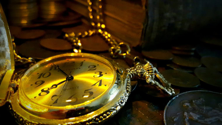 Antique pocket watch surrounded by coins and books